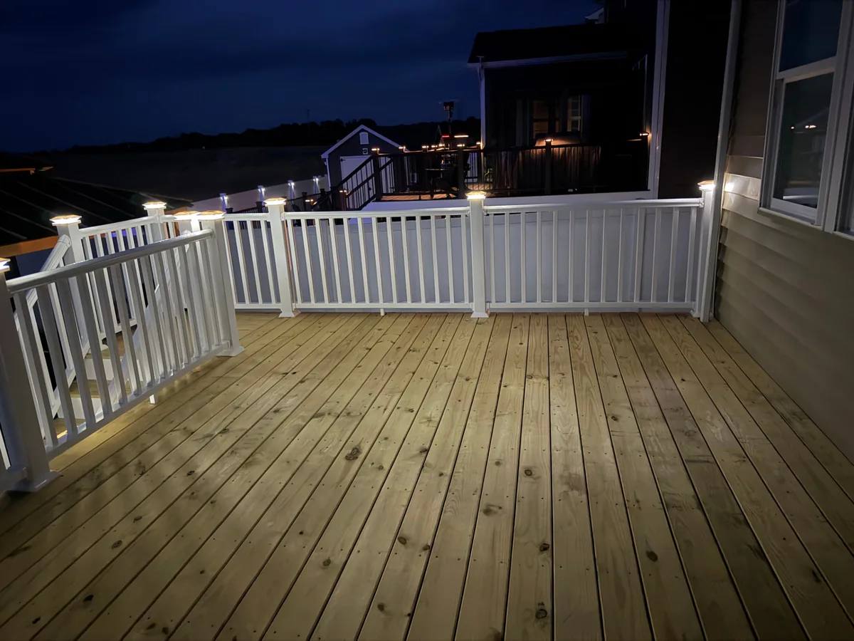 New wood deck with white vinyl railings and illuminated post cap lighting at dusk