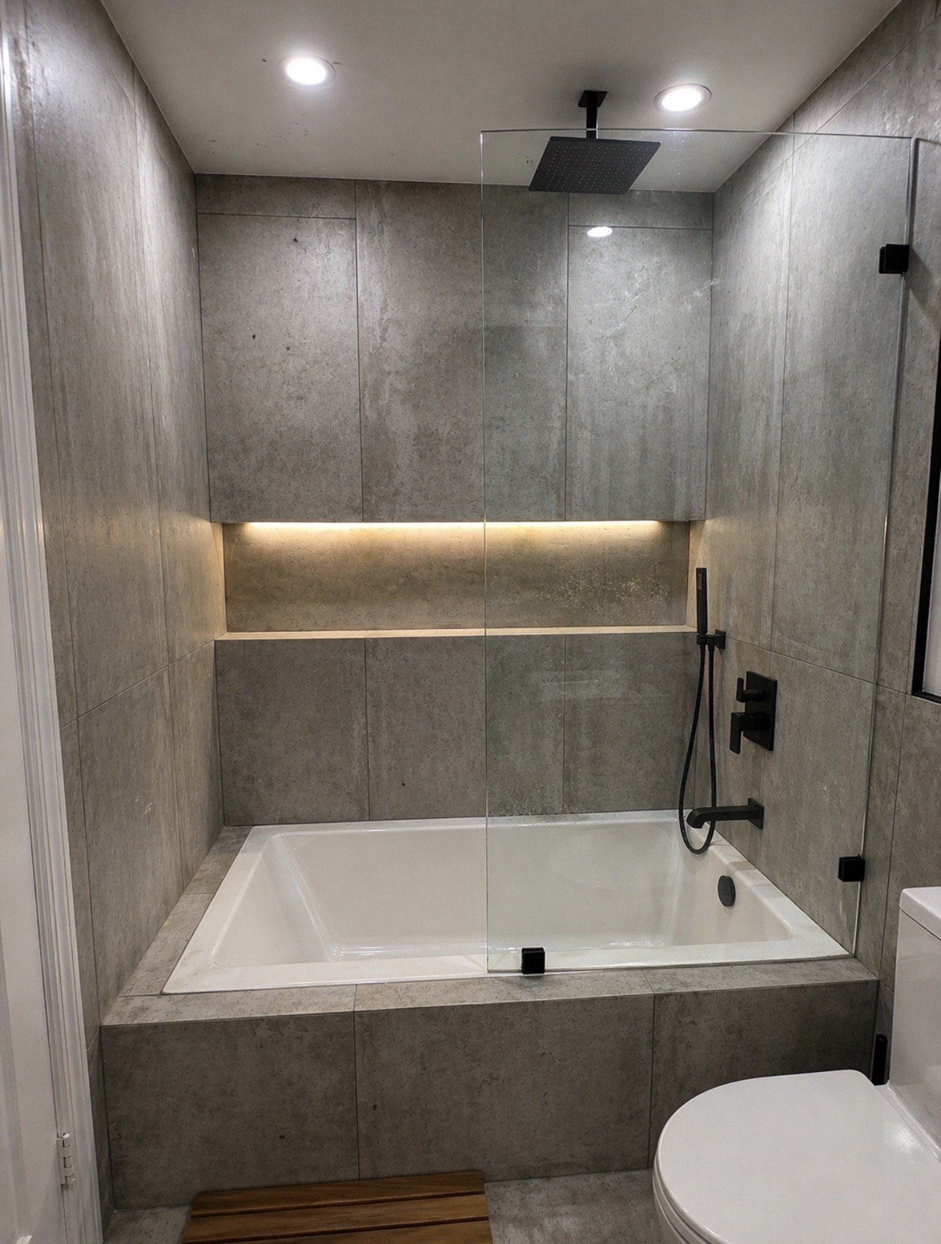 Arlington VA luxury bathroom remodel with gray stone tile, drop-in tub, lit niche, and matte black fixtures